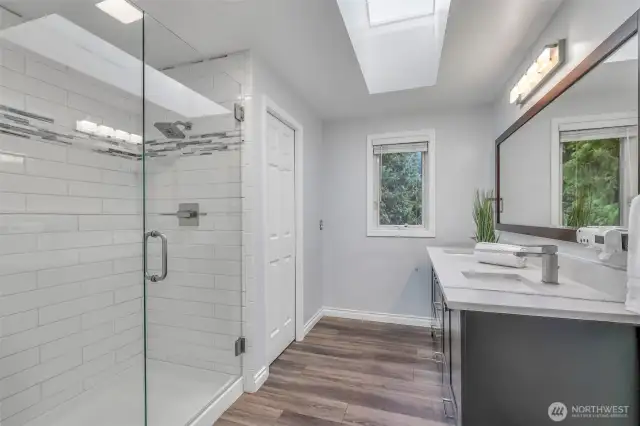 The luxurious primary bath is a modern retreat, featuring a frameless glass shower with dual shower heads, a double-sink vanity with quartz counters, and a skylight that fills the space with daylight.