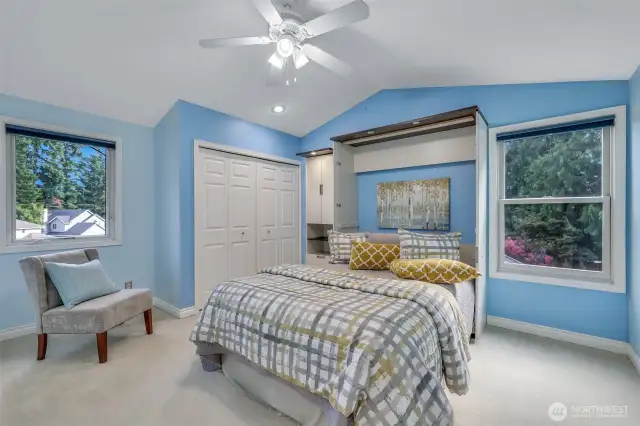 Vaulted ceilings and tree-lined views create a serene atmosphere in this generously sized fourth bedroom, which also includes a built-in storage nook for added convenience.