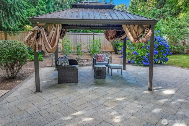 Enjoy gatherings in this inviting outdoor lounge space under a metal-roofed gazebo, with views of lush hydrangeas and garden beds all around.