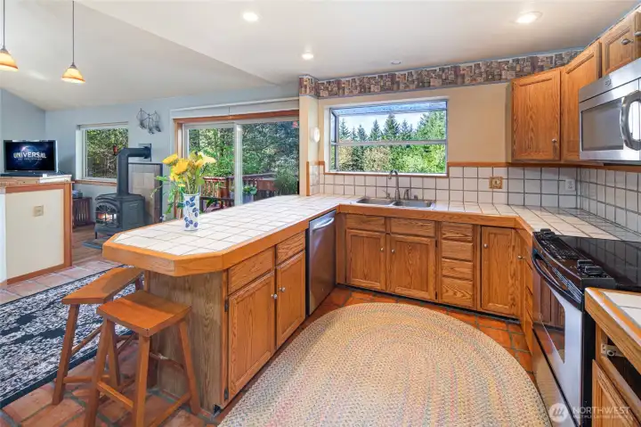 Bright and functional kitchen with large windows, tile countertops, and peaceful treetop views that bring the outdoors in.