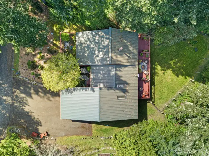 Overhead view highlights the home’s thoughtful layout, metal roof, attached garage, and inviting outdoor living spaces surrounded by nature.