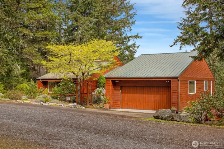 Charming front elevation showcases the home’s warm wood exterior, durable metal roof, and attached 2-car garage with ample parking.