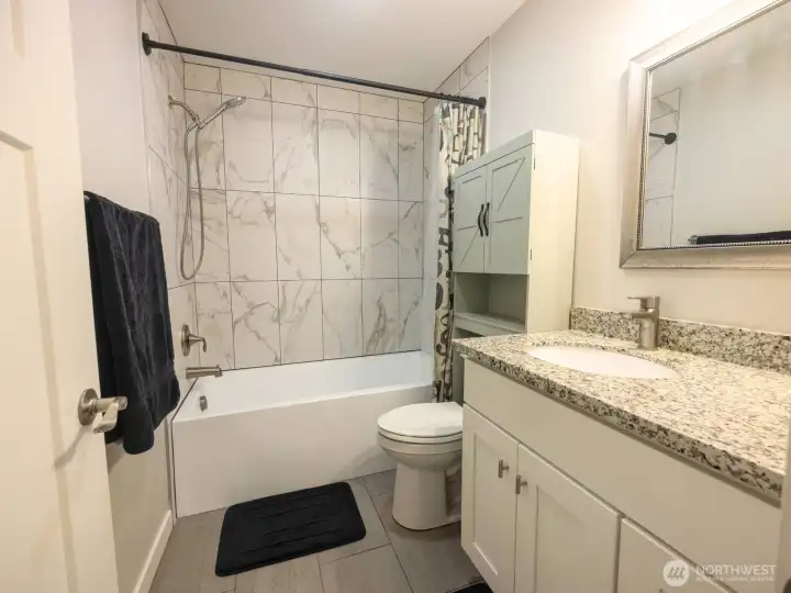 Stylish bathroom with granite counters, tile shower area and white cabinetry