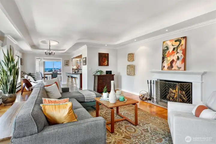 Large living room with hardwood floors, wood burning fire place, and a wall of windows with sweeping city views.
