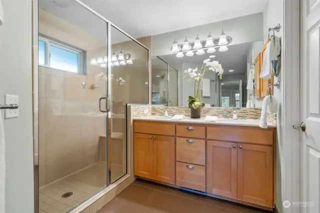 The spa-like primary bathroom includes a spacious glass-enclosed shower, dual vanity, and elegant finishes. Warm wood cabinetry, stylish tile accents, and a generous walk-in closet provide both charm and ample storage. Notice the six panel door here as you will throughout the home!