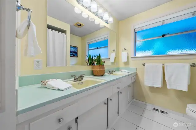 The main bathroom features a full tiled bath, a double vanity, and ample storage. Vintage tilework adds charm, while a large textured window for privacy!