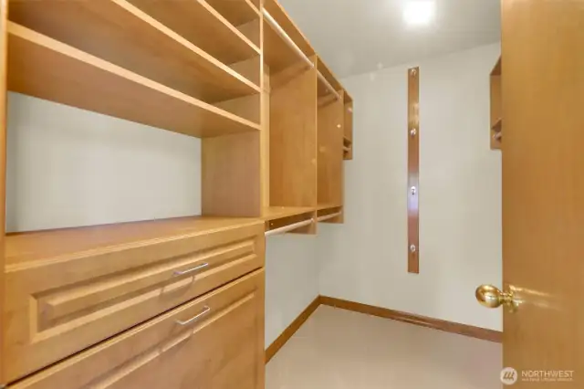 Primary suite closet with custom built-in shelving, drawers and hamper.
