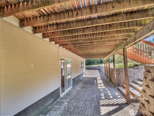 Large paved area below deck with entrance to daylight basement.