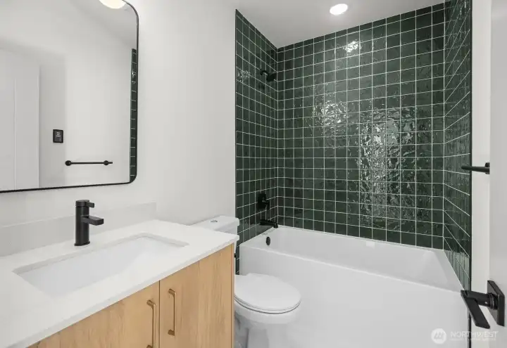 Striking full bath with designer black tile surround, sleek fixtures, and quartz-topped vanity.