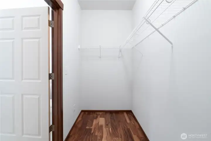 Spacious walk-in closet with shelving and acacia hard wood floors.
