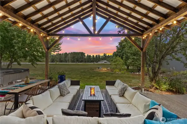 This stunning covered patio offers a perfect outdoor oasis, overlooking the expansive property. The spacious area is ideal for gatherings. The backyard features a cozy fire pit area that invites friends and family to enjoy warm evenings together. Along with the firepit there is a hot tub that provides a relaxing retreat, perfect for unwinding while taking in the scenic surroundings.