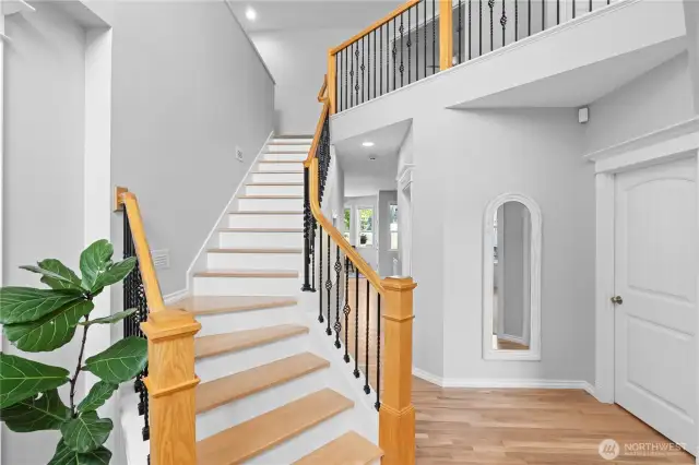 This grand entryway features soaring high ceilings that creat an open and airy atmosphere, complemented by stunning new wood floors that add warmth and sophistication. The elegant iron staircase and matching banister gracefully lead to the upper level, and make a beautiful focal point.