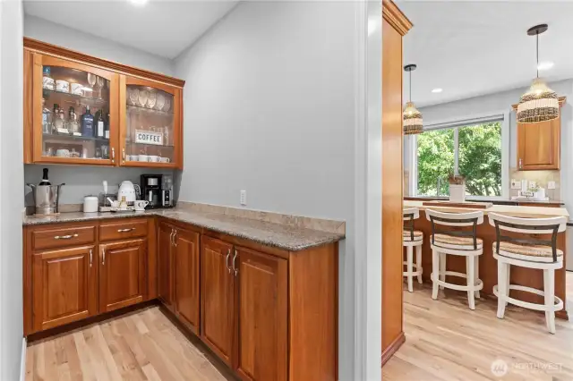 The butler's pantry has granite countertops and rich cherry wood cabinets, including upper glass-front cabinets that add a elegant touch. The wood flooring complements the cabinetry, creating a cohesive and inviting space.