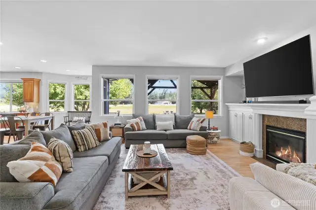 The family room features a wall of windows that flood the space with light. The focal point is a charming gas fireplace, surrounded by custom-built ins that provide elegant storage. The rich wood floors add warmth and character, enhancing the cozy and comfortable ambiance of the room. Wood-wrapped windows complement the overall design