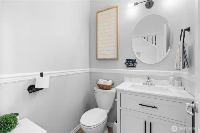 The charming powder room has tasteful chair rail molding and trim that add a refined touch to the space. The warm wood floors complement the elegant vanity. Great lighting enhances the room's inviting atmosphere.