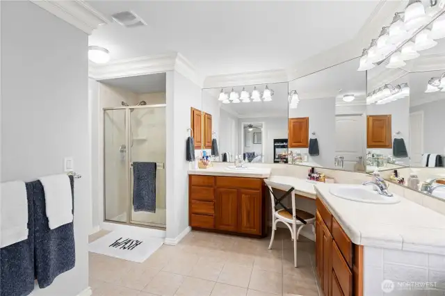 The primary suite offers a spacious and inviting atmosphere. The bathroom features double sinks set into beautiful tile countertops, complemented by rich cherry cabinets that add warmth. Large, impressive mirrors enhance the sense of space and brightness, beautifully illuminated by exceptional lighting. A dedicated makeup counter is situated between the double sinks adding convenience. The tile flooring completes the look, tying the elegant design together in this truly remarkable primary suite retreat