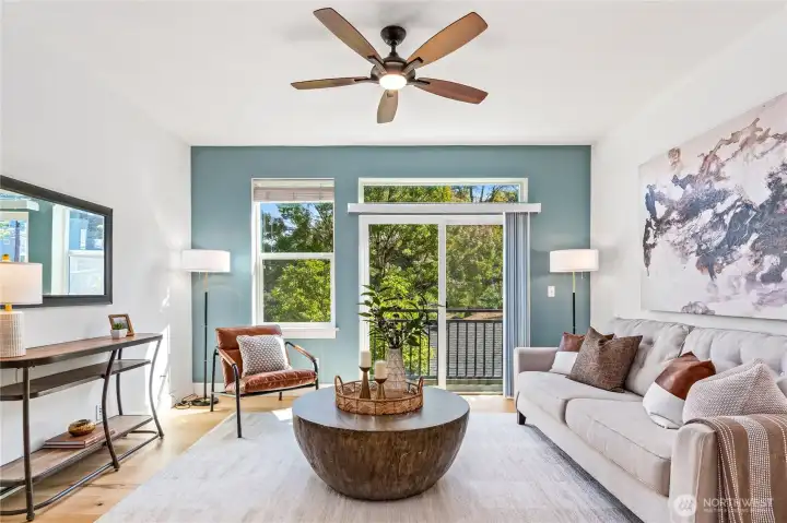 Bask in south-facing sunshine and breezes from the Juliet balcony, with views of trees and the patio below. A smoky blue accent wall and modern ceiling fan set the mood, while the sleek wood-and-concrete staircase anchors the space with architectural flair—making this living room as stylish as it is inviting.