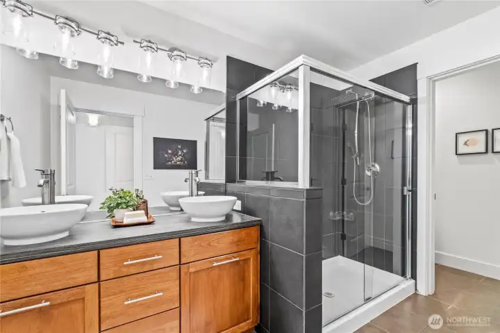 Directly connected to the primary—and with a second entry from the hall—this bathroom is equal parts stylish &   smart. Double vessel sinks top sleek cabinetry with loads of storage, while moody dark tiles set the tone. The   oversized shower features rainfall & handheld heads plus stainless shelves to keep your shower essentials   organized and within reach; a separate water closet (complete with outlet for a future bidet) adds function   with a wink of luxury.