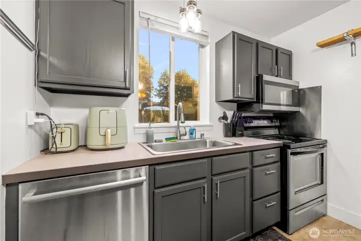 The kitchen is equipped with sleek stainless steel appliances and a dedicated workspace. A window over the sink lets in natural light and provides a pleasant view while you wash dishes.