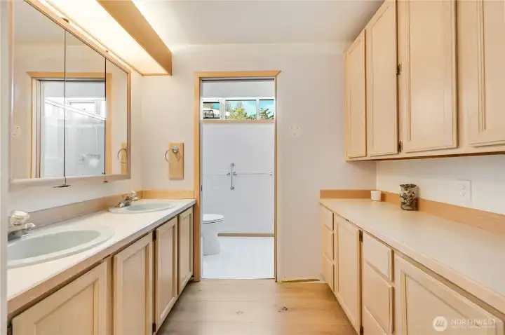 The primary bathroom is the only area that has not been remodeled in this house. A row of closet on the RH side, and there's plentiful cabinet storage. A private toilet and shower room is on the left-side background.