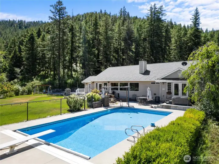 Private Cashmere retreat featuring a heated in-ground pool, spacious patio, and hot tub, all set against a backdrop of mature pines and scenic mountain views. Fully usable grounds offer a perfect blend of recreation, relaxation, and privacy.