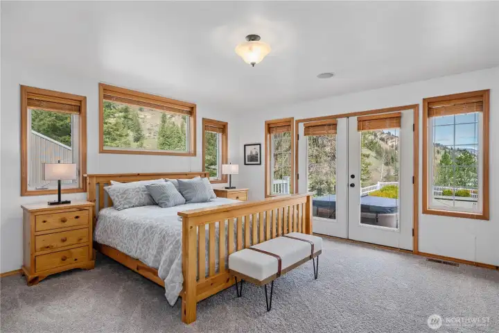 Serene primary suite filled with natural light, featuring multiple windows capturing peaceful hillside views and private access to outdoor living