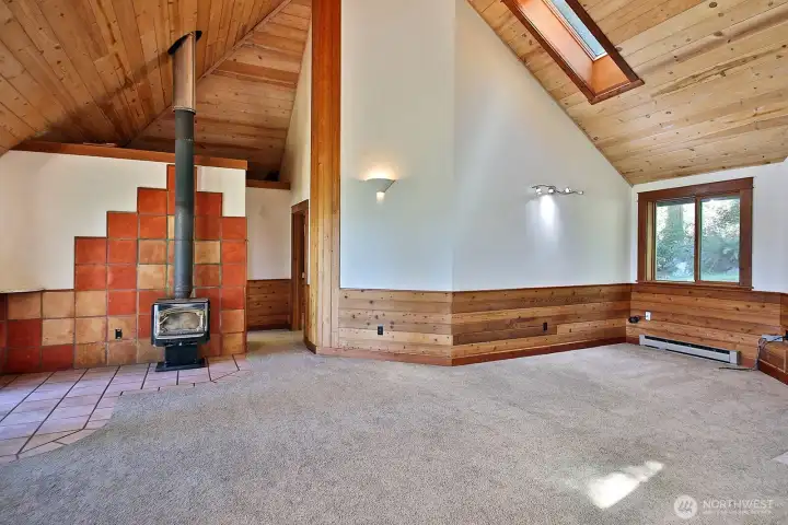Vaulted ceilings with skylights and beautiful wood accents throughout. A wood stove and newer carpet. The other bedroom and main level full bath are beyond the wood stove. Bedroom to the right, bathroom to the left.