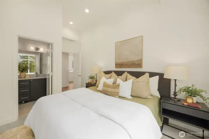 Serene primary retreat featuring a spacious, light-filled layout, pristine neutral tones, and expansive windows framing peaceful greenery.