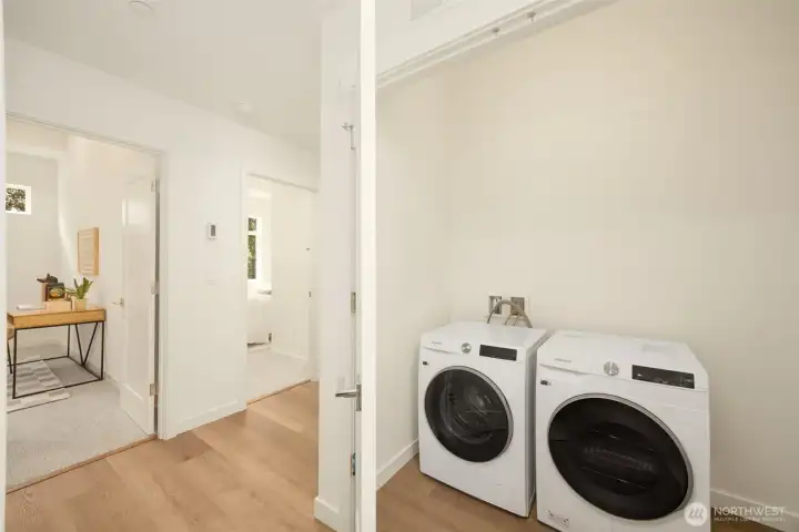 Dedicated upper-level utility and laundry space equipped with a premium front-loading washer and dryer set, custom white cabinetry, and functional layout.