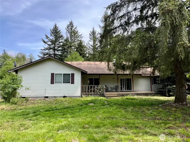 Front view of the home highlighting the front entry, and peaceful natural setting. Surrounded by mature trees and open green space, this image captures the inviting rural charm and privacy the property offers.