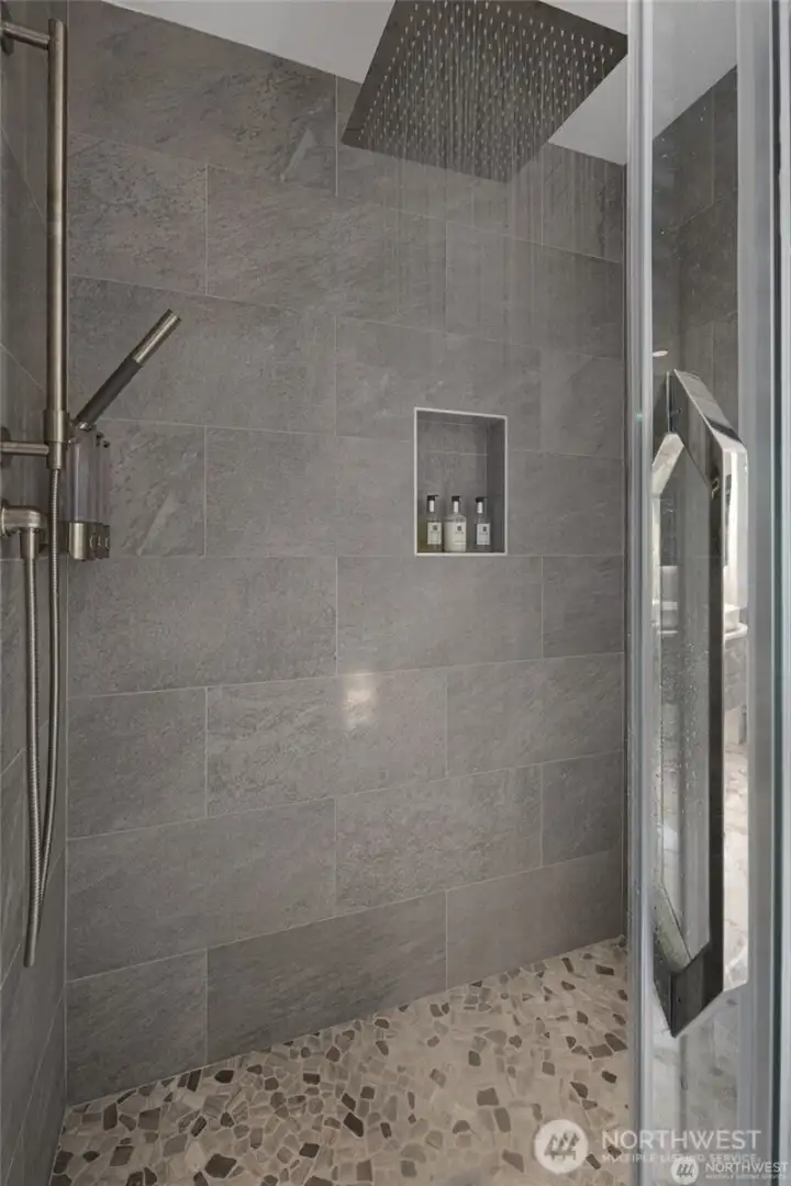A tiled walk-in shower with a rainfall-style showerhead, hand sprayer, and built-in niche adds a luxurious spa-like touch to the primary suite. A tiled walk-in shower with a rainfall-style showerhead, hand sprayer, and built-in niche adds a luxurious spa-like touch to the primary suite.