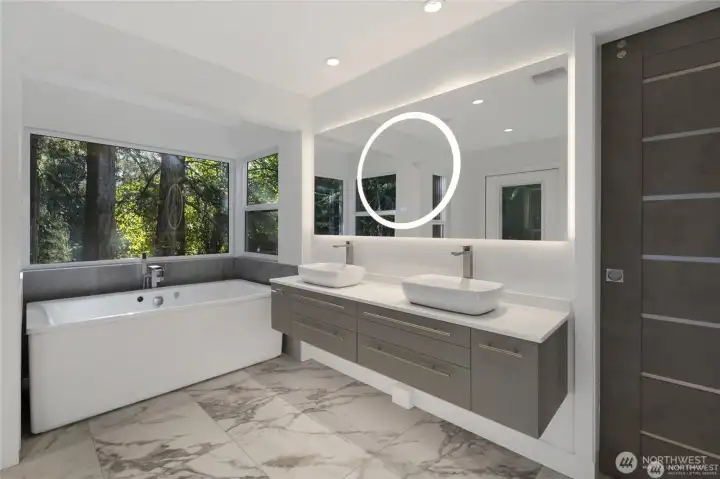 The spa-inspired primary bath offers a soaking tub, dual vessel sinks, sleek cabinetry, heated-look tile styling, and a peaceful view into the trees. The spa-inspired primary bath offers a soaking tub, dual vessel sinks, sleek cabinetry, heated-look tile styling, and a peaceful view into the trees.