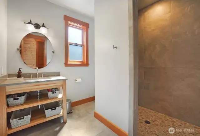 Hallway bathroom on the main floor features a custom, handmade vanity, walk in shower, and large format tiles on floor and shower.