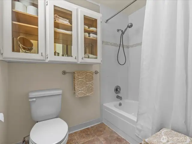 Full bathroom toilet and tub / shower.  The glass doored cabinet with a mirrored back is elegant and useful bathroom storage.
