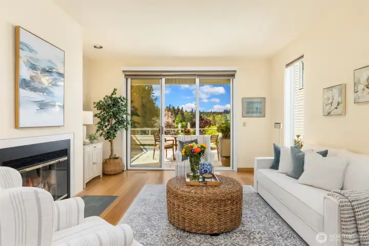 Mainfloor living room with wood burning fireplace, sliding doors to terrace over-looking views of water, gardens and soaring evergreens.