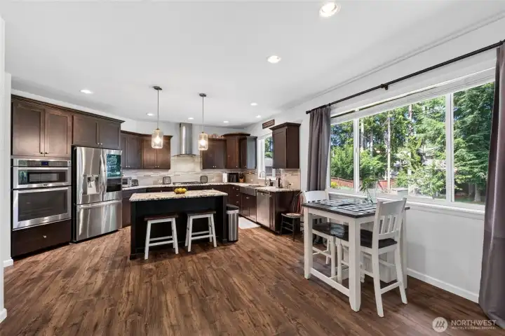 Open-concept kitchen and dining area feature expansive windows overlooking the park-like backyard, creating a bright and inviting space for everyday living.