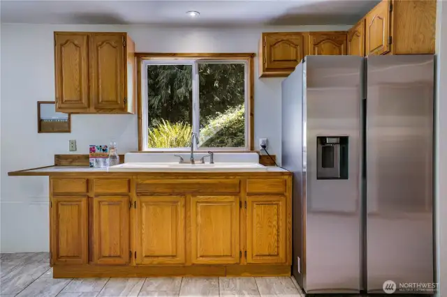 Garden-level kitchenette ready for canning, hobbies, or a secondary living setup—complete with stainless fridge and views of the backyard.