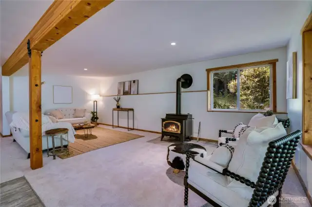 Cozy daylight basement living space with a freestanding wood stove, natural light, and flexible zones for lounging, media, or games.
