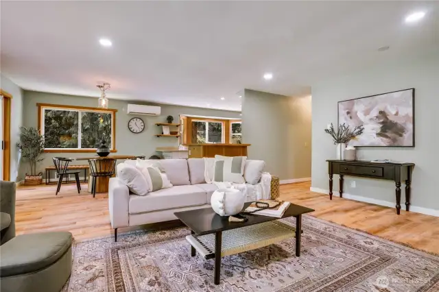 Open-concept layout connects living, dining, and kitchen areas with seamless flow, wood flooring, and soft forest-inspired tones throughout.