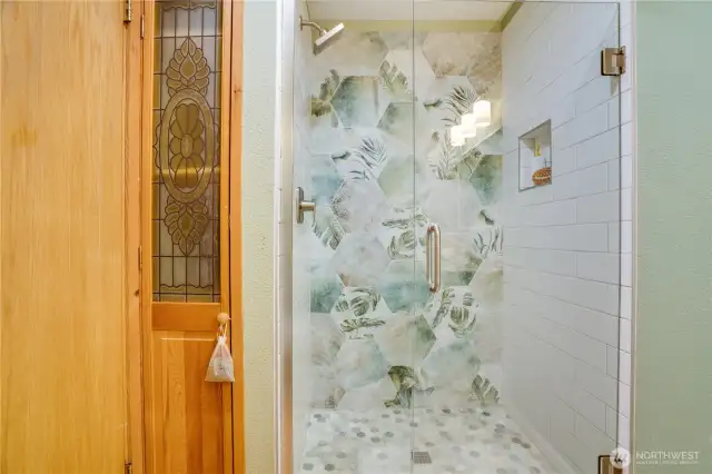 The main bath has a spa-inspired shower retreat featuring vibrant botanical tilework, glass surround, and modern fixtures.