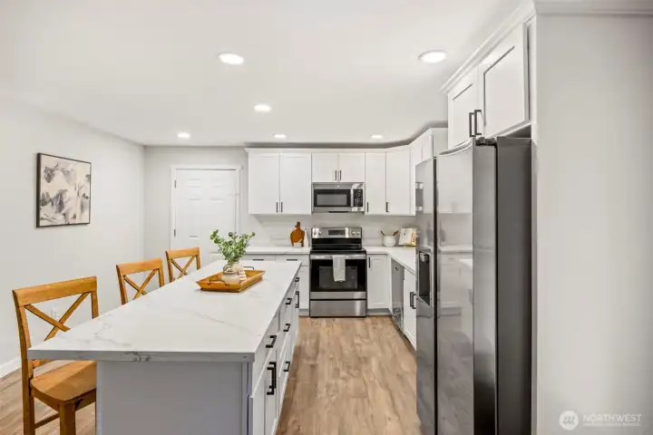 Kitchen with quartz counters, white cabinets, stainless steal appliances  & large island with seating