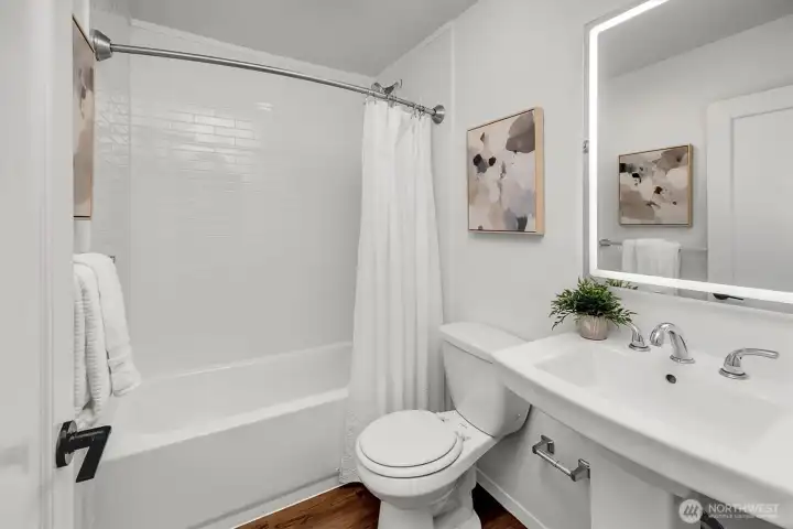 Main floor full bath with lovely new designer tile surround, new bathtub and dimmable LED vanity mirror.
