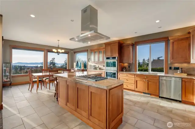 Natural light pours into the expansive kitchen and dining area, highlighting custom cabinetry, a large center island, and picturesque water and island views.