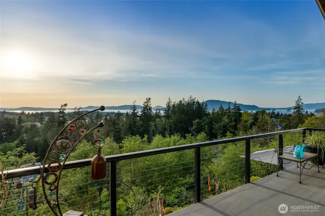 The expansive deck showcases sweeping views of lush evergreens, sparkling waterways, and distant islands.