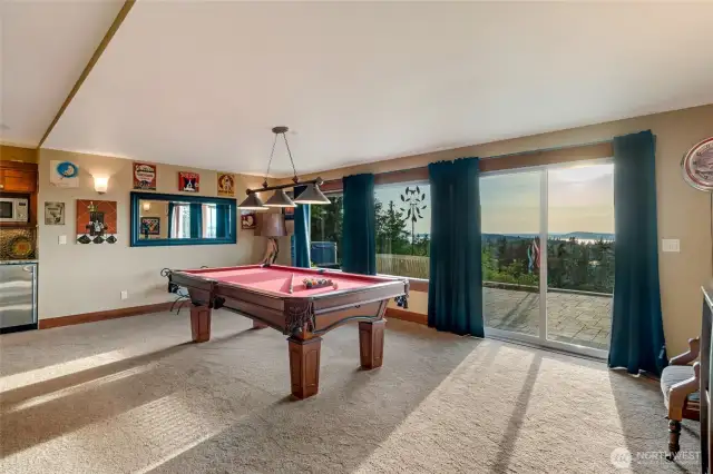 The game room features a pool table, a wet bar, and large windows that open to patio access and sweeping sunset views.