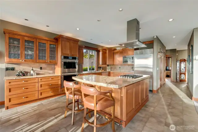 A chef’s kitchen featuring rich wood cabinetry, granite countertops, a spacious center island with seating, and premium stainless steel appliances.