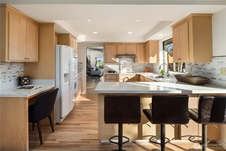 This bright kitchen features a separate cooktop, double wall ovens, a breakfast bar, quartz counters with tile backsplash and an undermount sink.