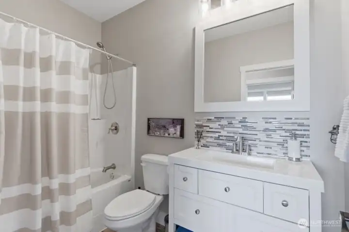 A full bath with tub and shower and tile backsplash on the vanity.