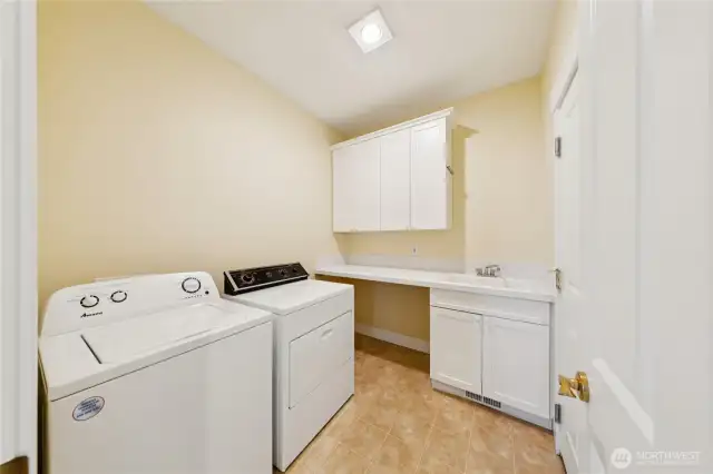 Separate laundry room equipped with a full-size washer and dryer, built-in folding counter, and utility sink for added convenience.