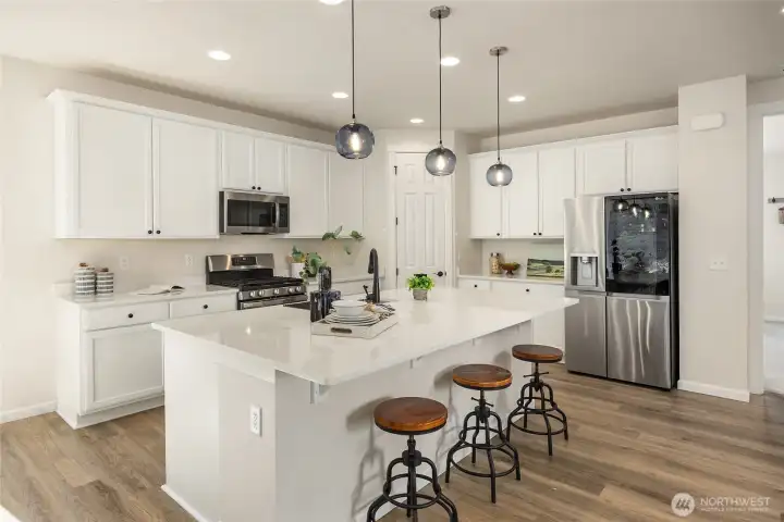 The large chef's kitchen with tall shaker-style white cabinetry and large corner closet-style pantry, features elegant pendant lighting over the large island with breakfast bar. Notice the high-end LG french door refrigerator with ice and water in the door and see-through panel door so you can see the contents without opening the door.
